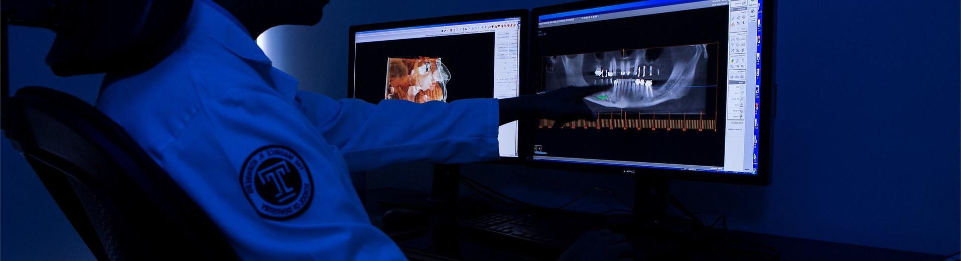 一名牙科男学生正在电脑屏幕上看牙科x光片.