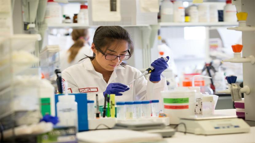 一名女生物系学生穿着实验服，戴着护目镜，在坦普尔大学的一个研究实验室里进行实验.