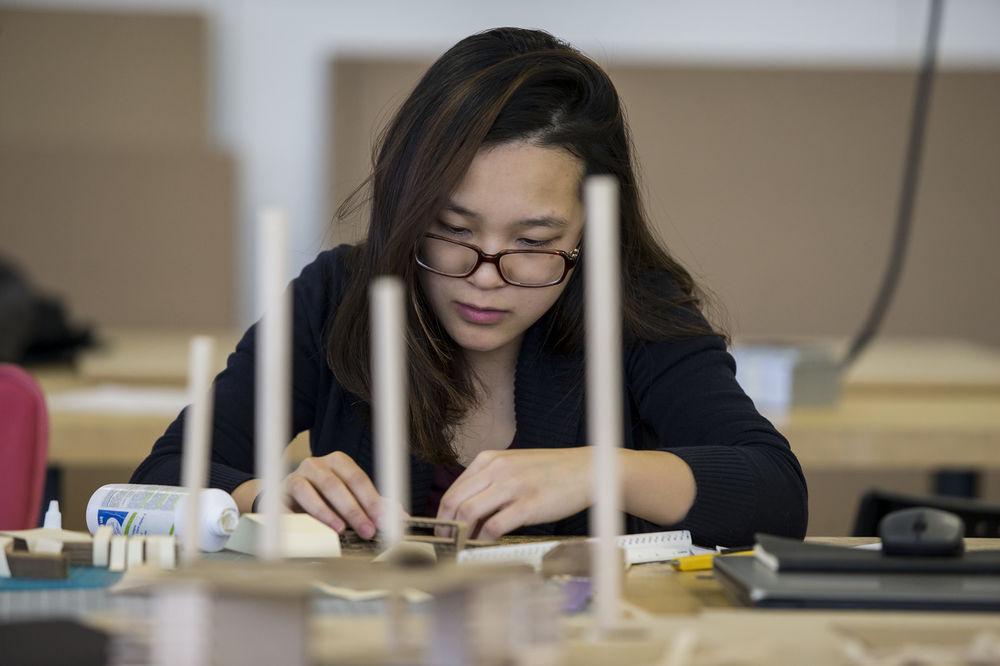 一个黑发戴眼镜的女人在一张放着小纸板的桌子前工作.